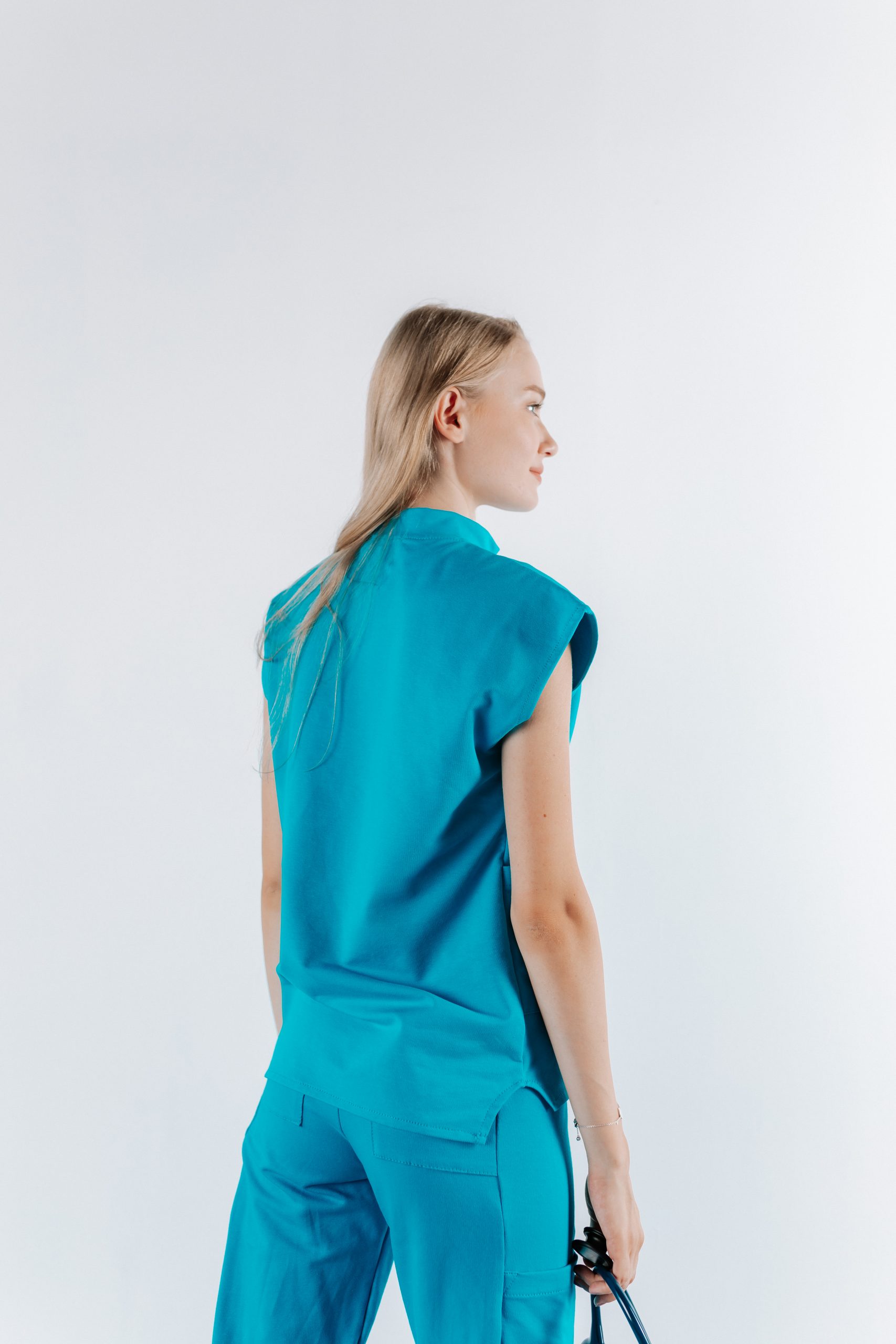 Vedere din spate a unei doamne doctor ce poarta o bluza tunica de scrub medical albastru azure.Uniforma medicala albastru azure este din bumbac 95% si elastan 5% cu croiala fit.