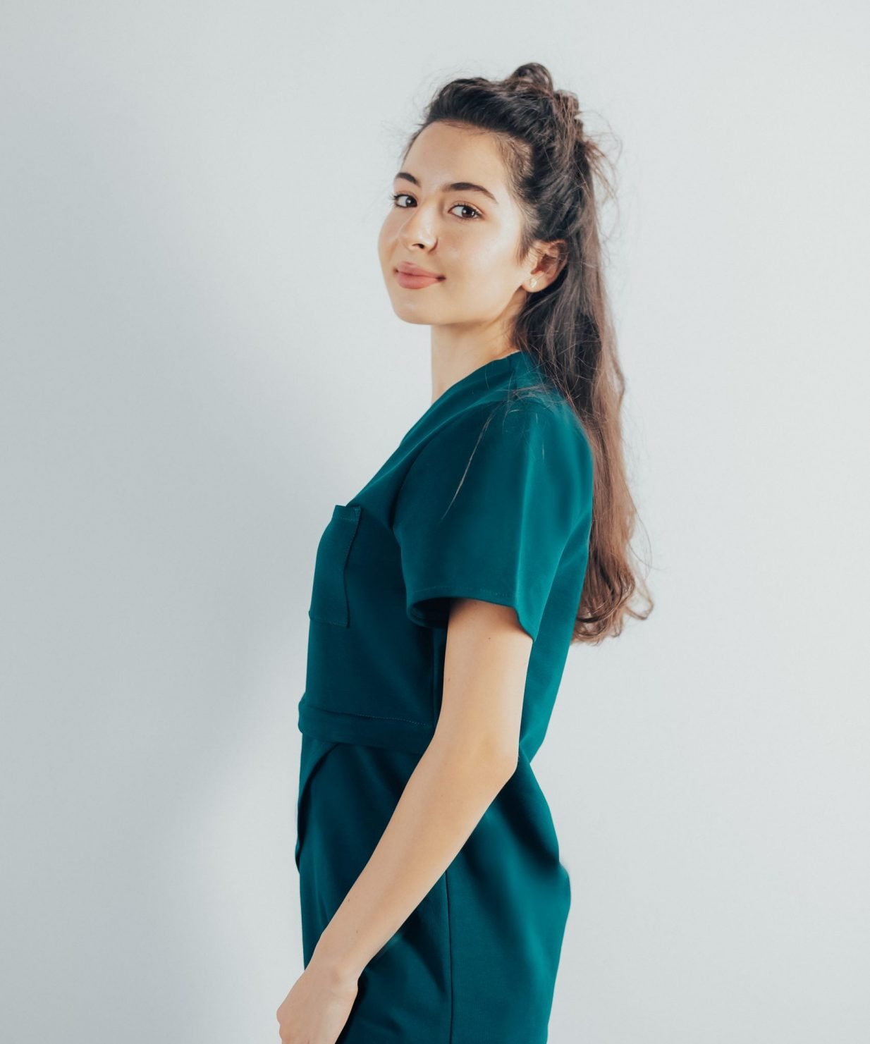 Fotografie cu vedere din lateral a unei studente la medicina in timp ce poarta o bluza edgy de scrub medical turcoaz inchis ce reprezinta uniforma medicala reprezentativa a unui doctor