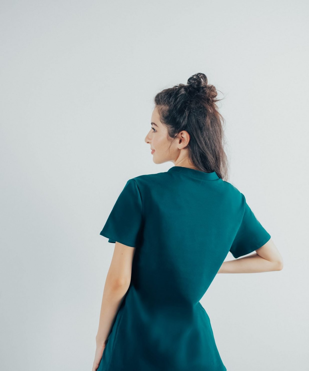 Fotografie cu vedere din spate a unei studente la medicina in timp ce poarta o bluza edgy de scrub medical turcoaz inchis ce reprezinta uniforma medicala reprezentativa a unui doctor