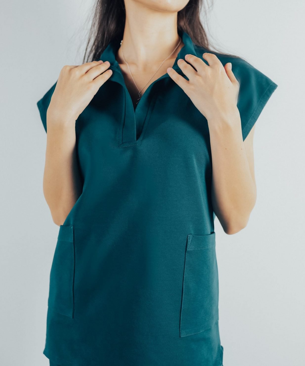 Fotografie cu vedere din fata a unei studente la medicina in timp ce poarta o bluza tunica de scrub medical turcoaz inchis ce reprezinta uniforma medicala reprezentativa a unui doctor