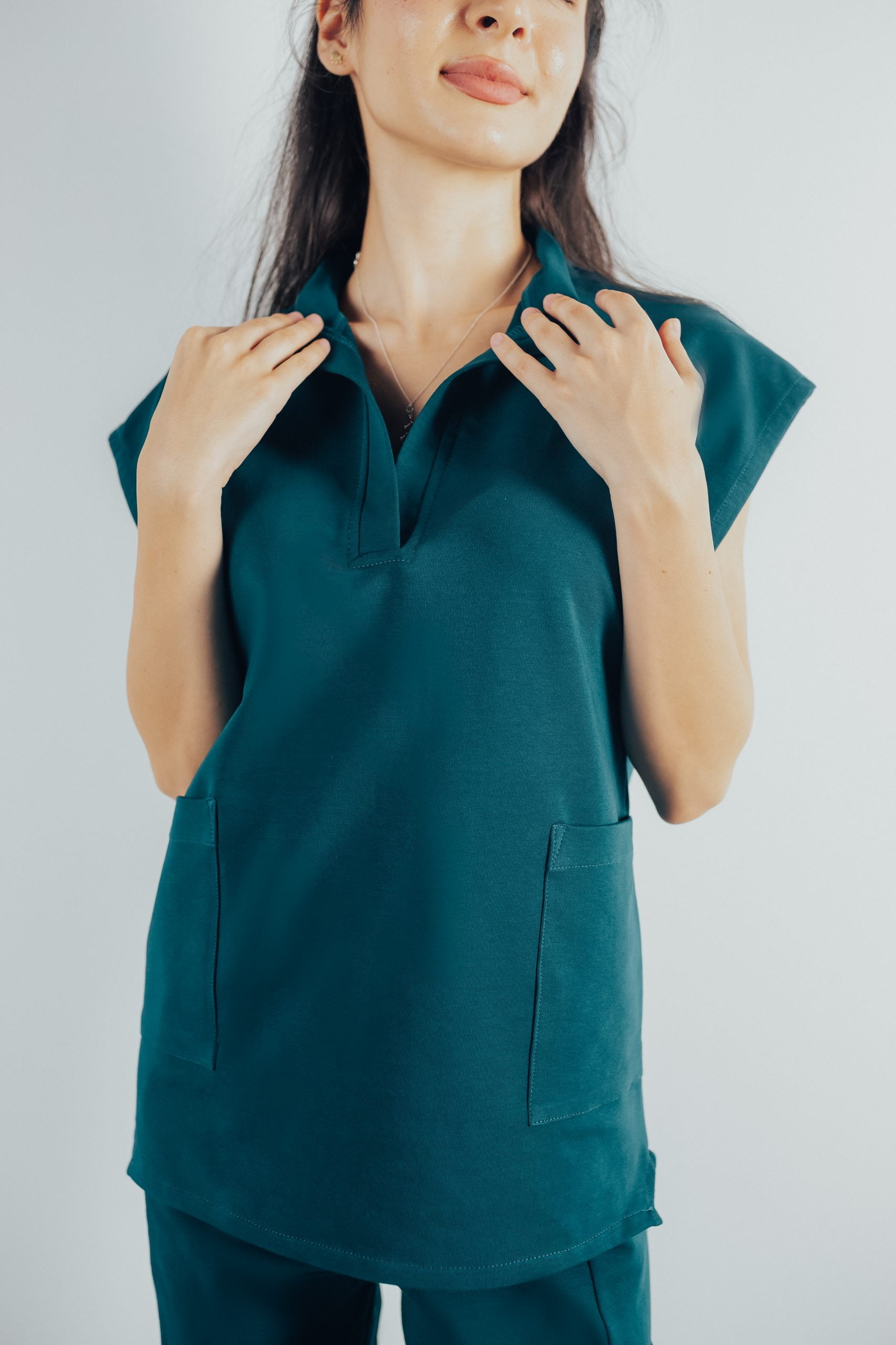 Fotografie cu vedere din fata a unei studente la medicina in timp ce poarta o bluza tunica de scrub medical turcoaz inchis ce reprezinta uniforma medicala reprezentativa a unui doctor